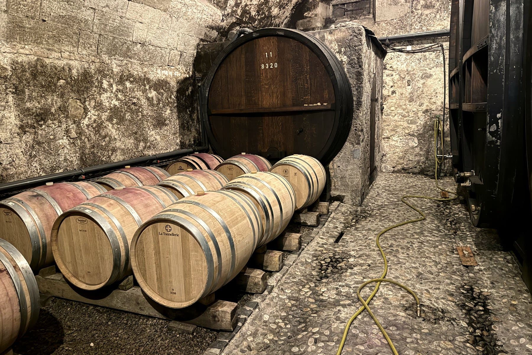 Des barriques de chêne alignées sous la voûte de pierre de la cave du Château de Vinzel.