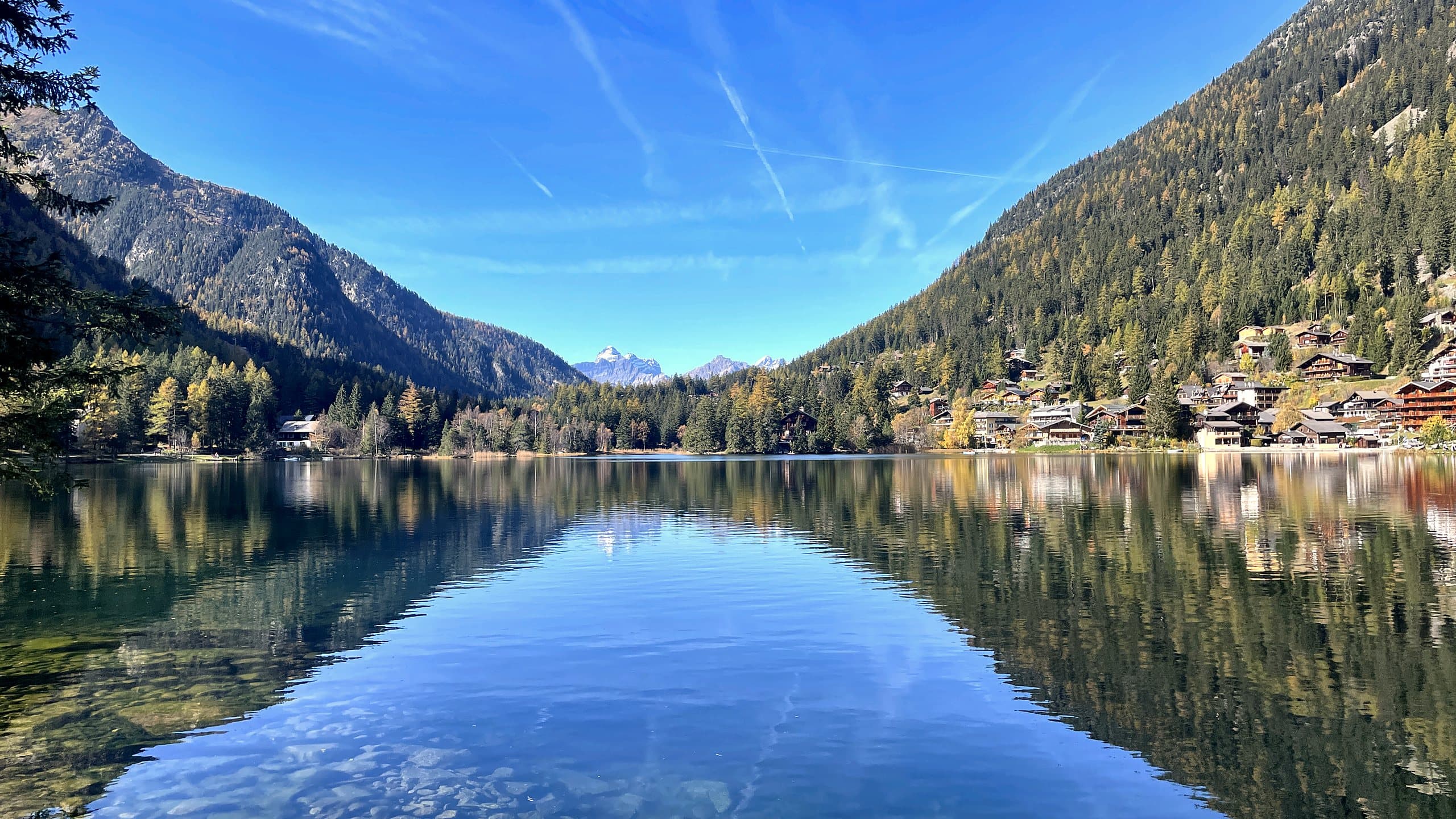 Le lac de Champex en automne, les mélèzes et les chalets reflétés dans l'eau.