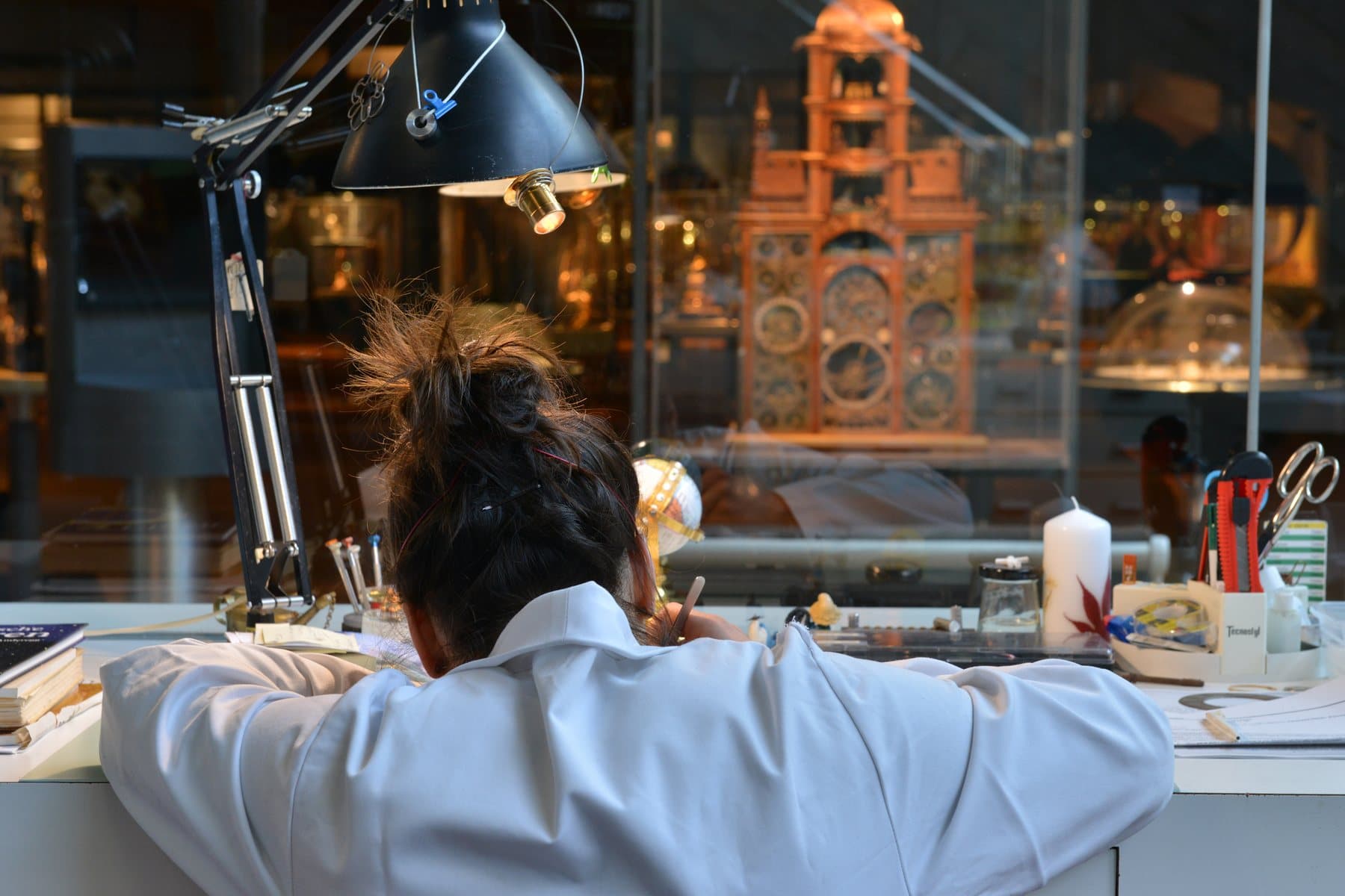 Une restauratrice au travail dans l'atelier du Musée international d'horlogerie, devant une grande horloge.