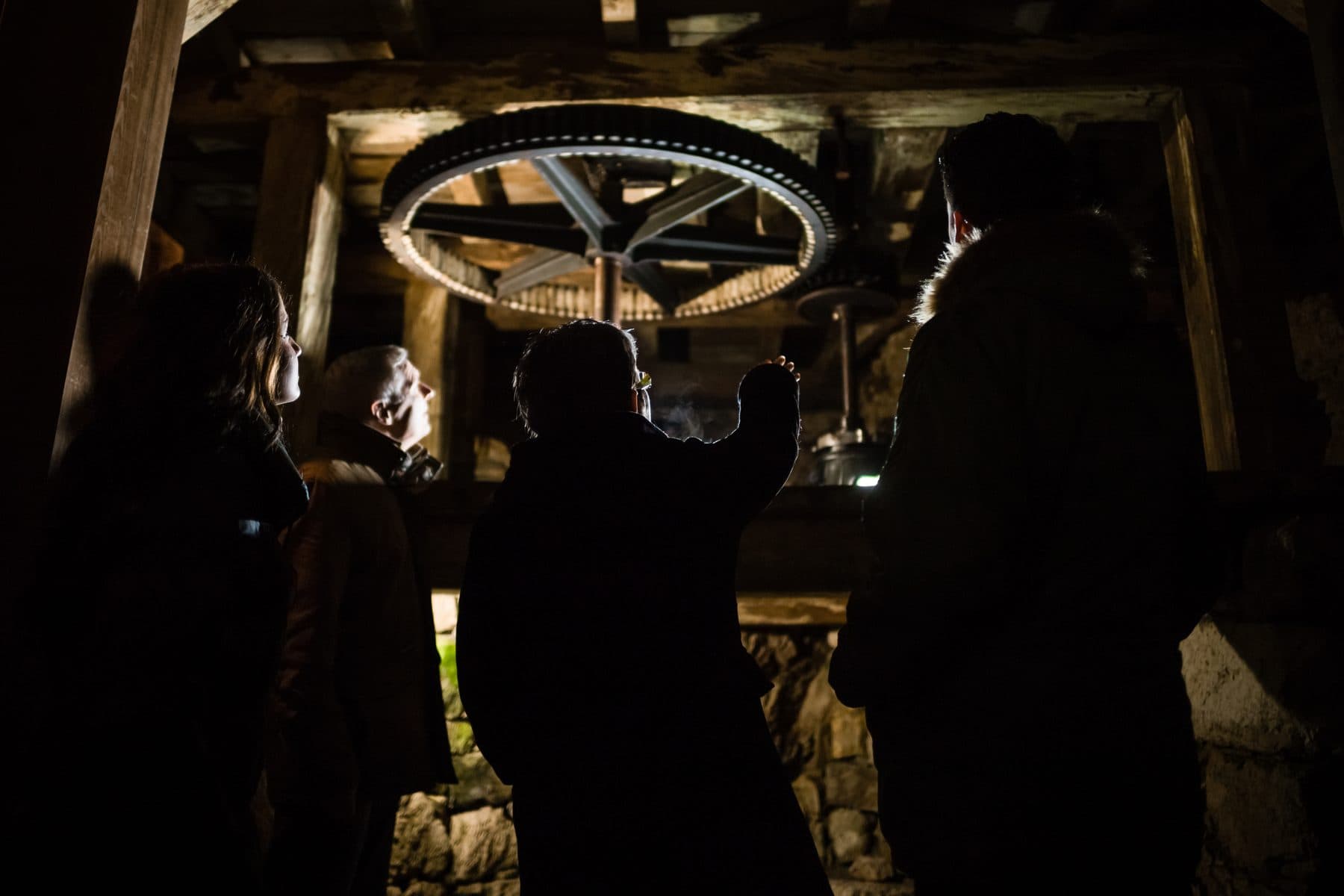 Des visiteurs, à contre-jour, devant une grande roue dentée des Moulins souterrains.