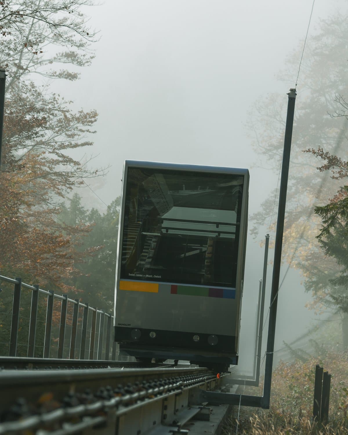 La voiture du funiculaire qui monte dans le brouillard, entre les arbres d'automne.