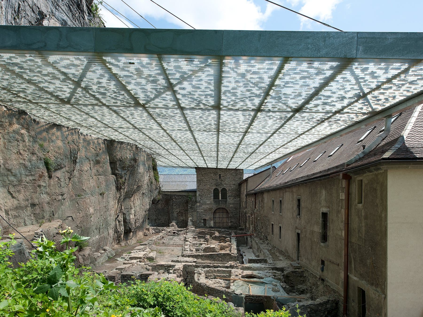 Le site archéologique du Martolet, ses murs anciens sous une couverture translucide, entre la falaise et l'abbaye.