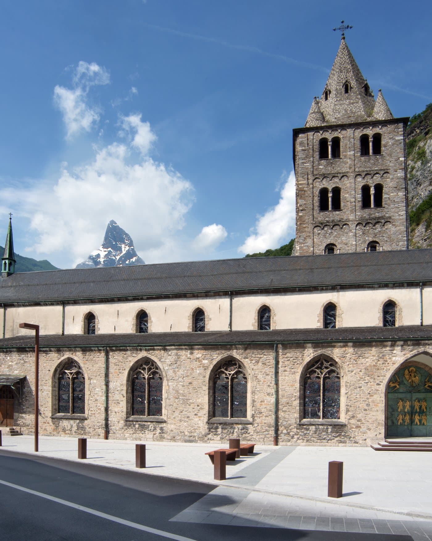 La basilique et le clocher de l'abbaye de Saint-Maurice adossés à la falaise, sous un ciel bleu.