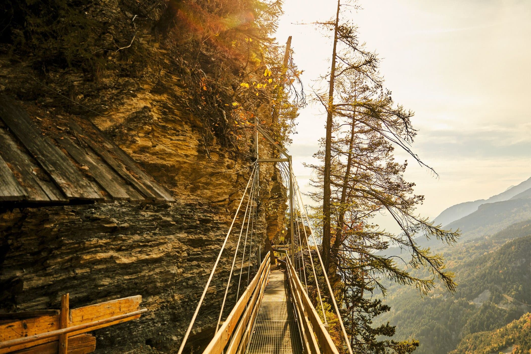 Le chemin du bisse du Torrent-Neuf accroché à la paroi, le canal de bois et la passerelle au-dessus du vide, en automne.