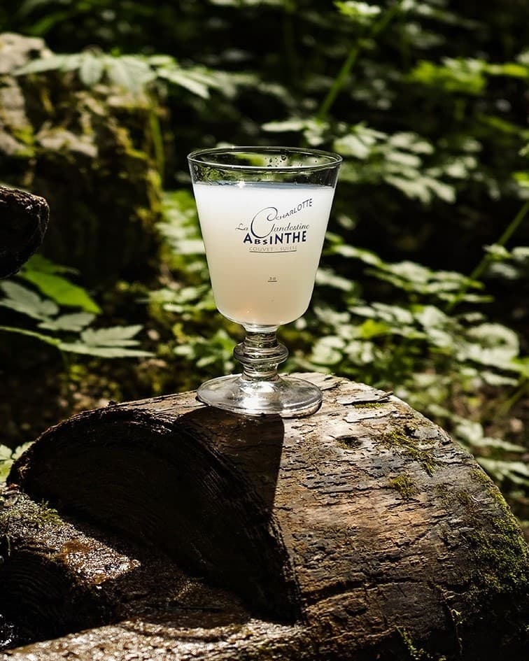 Un verre d'absinthe La Clandestine, troublée par l'eau, posé sur un tronc dans la forêt.